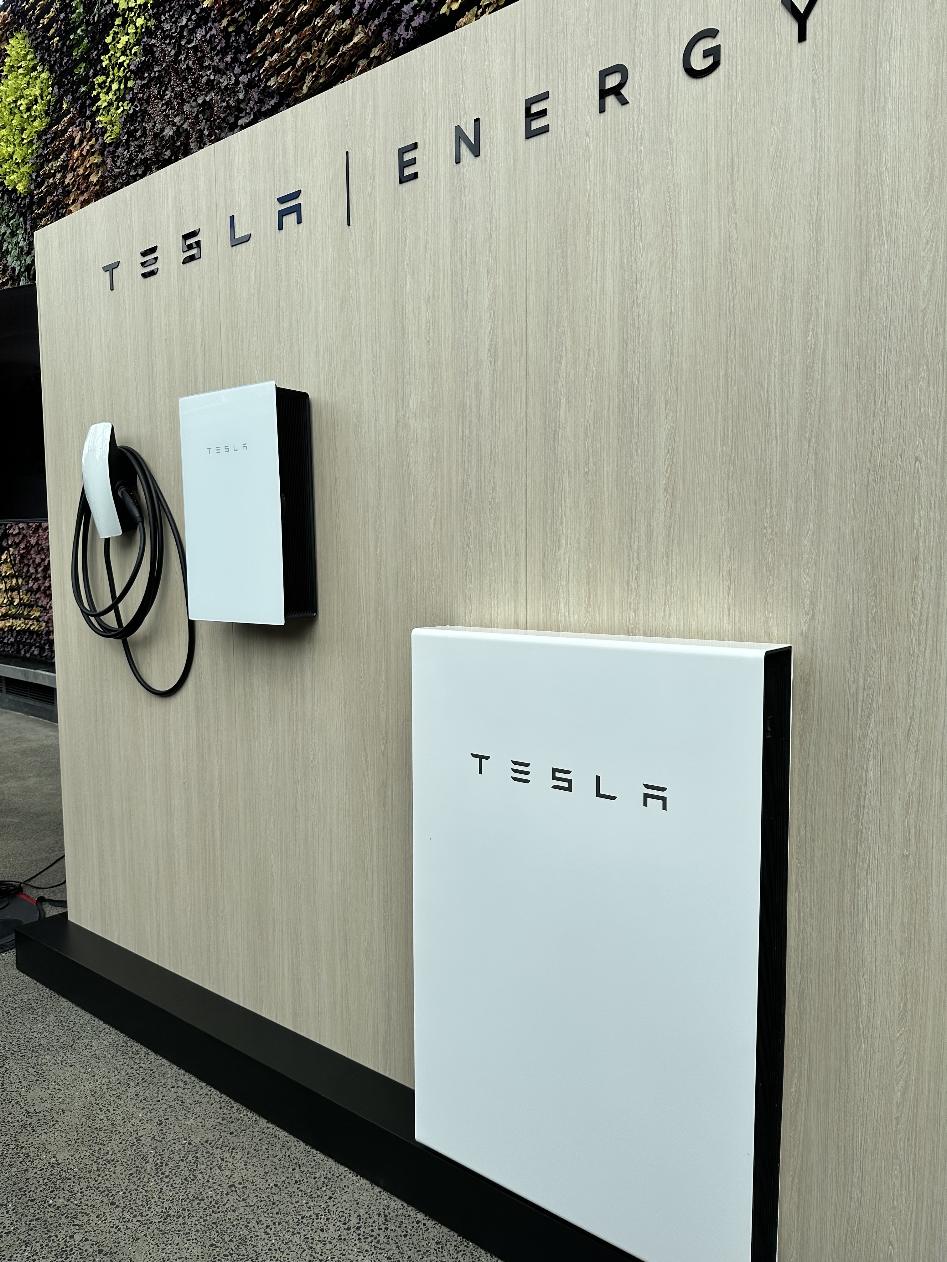 Tesla battery and EV charging equipment on a showroom display wall
